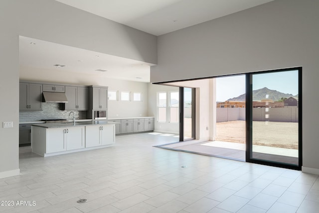 kitchen with gray cabinetry, a mountain view, a high ceiling, a center island with sink, and tasteful backsplash