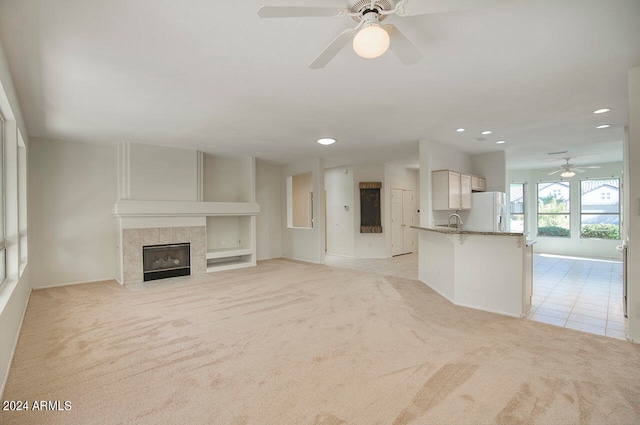 unfurnished living room featuring light carpet, a fireplace, ceiling fan, and sink