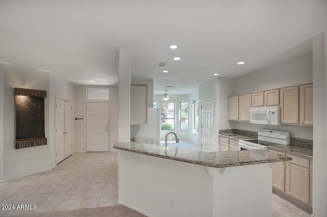 kitchen featuring white appliances, a breakfast bar, light stone counters, sink, and kitchen peninsula