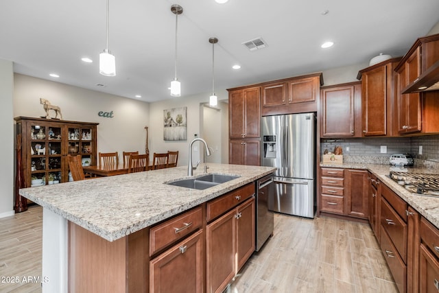 kitchen featuring sink, a kitchen island with sink, backsplash, stainless steel appliances, and decorative light fixtures