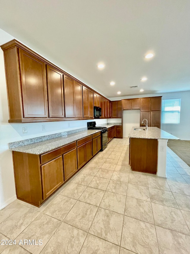 kitchen featuring a kitchen island with sink, black appliances, sink, light tile patterned floors, and light stone countertops