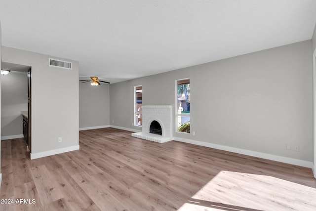 unfurnished living room featuring ceiling fan, a brick fireplace, and light hardwood / wood-style flooring