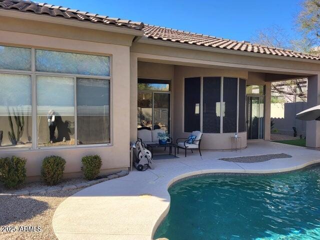 back of property featuring a patio, a tile roof, an outdoor pool, stucco siding, and a sunroom