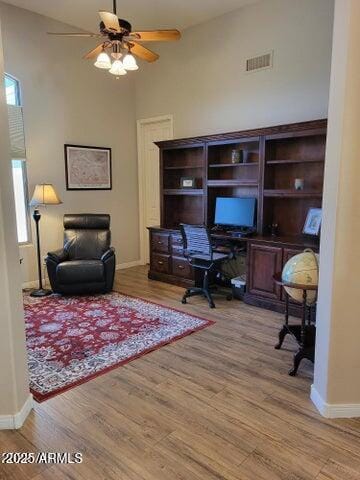 office space featuring wood finished floors, ceiling fan, baseboards, visible vents, and a high ceiling