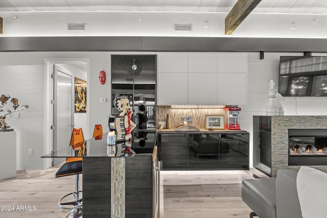 kitchen with decorative backsplash, white cabinetry, beamed ceiling, and light wood-type flooring