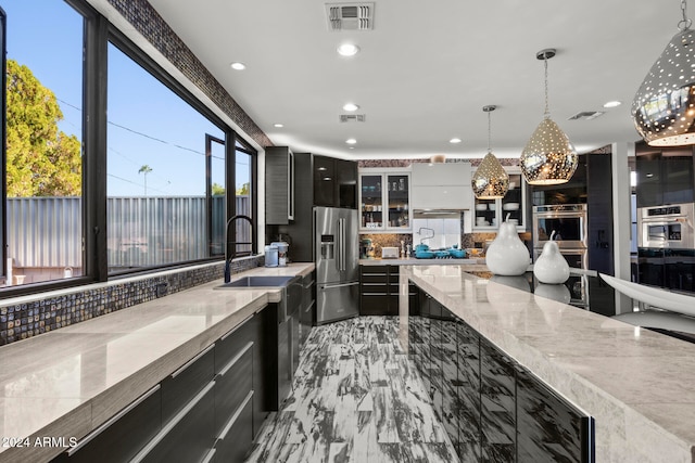 kitchen featuring pendant lighting, light stone counters, backsplash, and appliances with stainless steel finishes