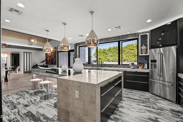 kitchen with sink, hanging light fixtures, light hardwood / wood-style floors, high quality fridge, and a kitchen island