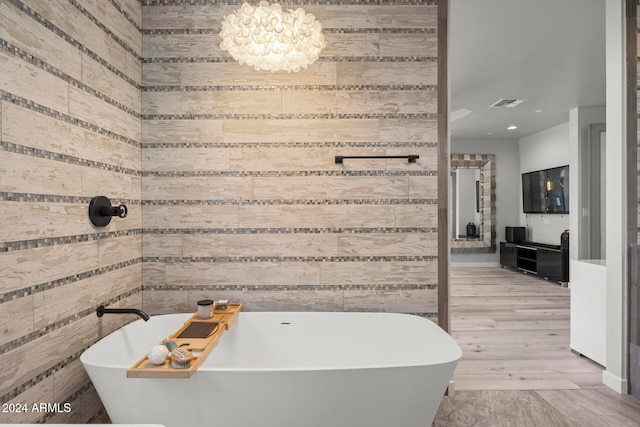 bathroom featuring a chandelier, wooden walls, a bath, and hardwood / wood-style flooring