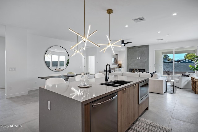 kitchen featuring a center island with sink, stainless steel appliances, a fireplace, pendant lighting, and sink