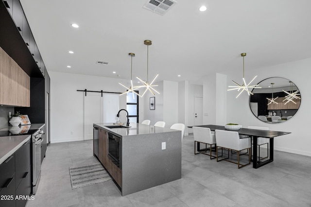 kitchen featuring decorative light fixtures, appliances with stainless steel finishes, a kitchen island with sink, and a barn door