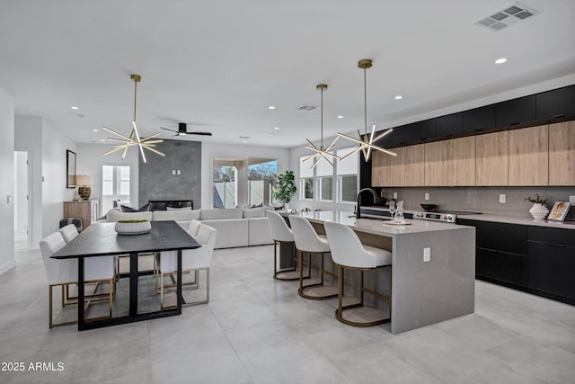 kitchen with a fireplace, sink, hanging light fixtures, an island with sink, and a kitchen breakfast bar