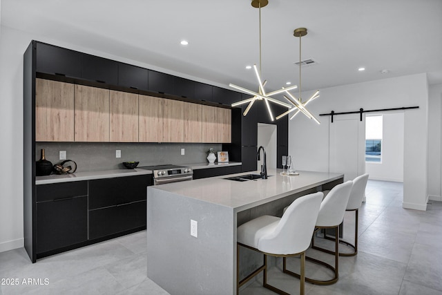 kitchen with decorative light fixtures, a barn door, stainless steel electric range, sink, and a kitchen island with sink