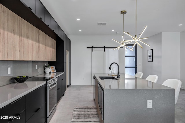 kitchen with a barn door, an island with sink, sink, hanging light fixtures, and stainless steel electric range