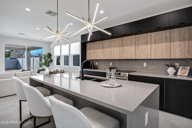 kitchen featuring a center island with sink, decorative backsplash, sink, a kitchen breakfast bar, and a chandelier