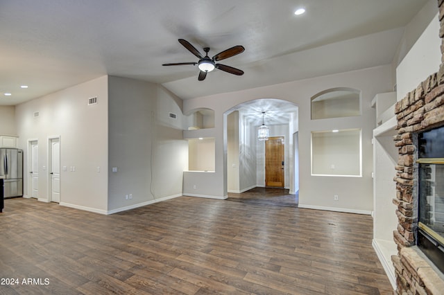 unfurnished living room featuring a stone fireplace, lofted ceiling, dark wood-type flooring, and ceiling fan