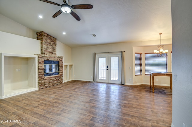 unfurnished living room with wood-type flooring, vaulted ceiling, ceiling fan with notable chandelier, a stone fireplace, and french doors