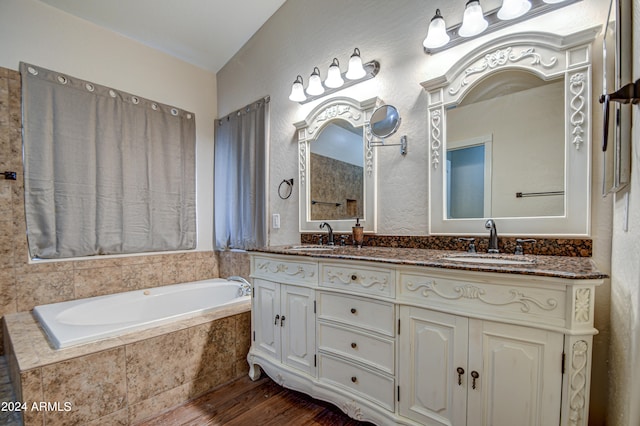 bathroom with vanity, wood-type flooring, tiled tub, and vaulted ceiling