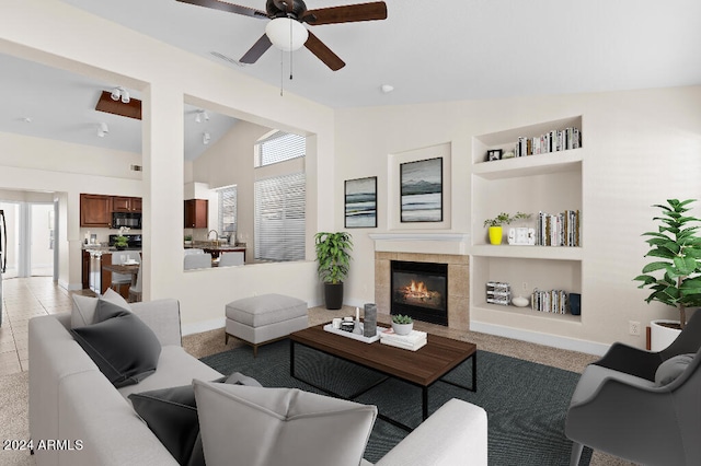 living room with lofted ceiling, ceiling fan, light tile flooring, a tile fireplace, and built in shelves