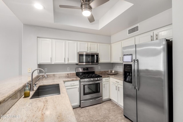 kitchen with a raised ceiling, visible vents, appliances with stainless steel finishes, white cabinets, and a sink