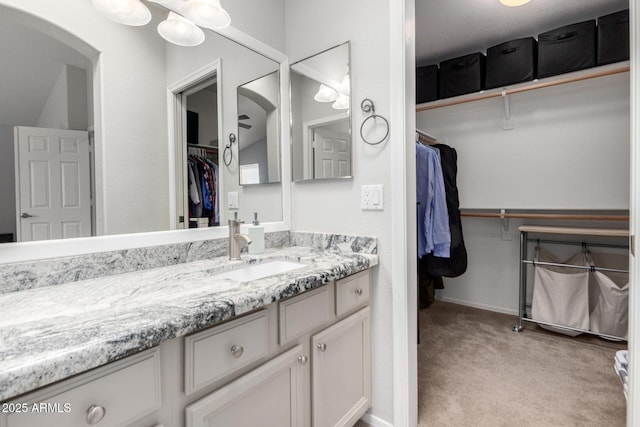 bathroom with a walk in closet, vanity, and baseboards