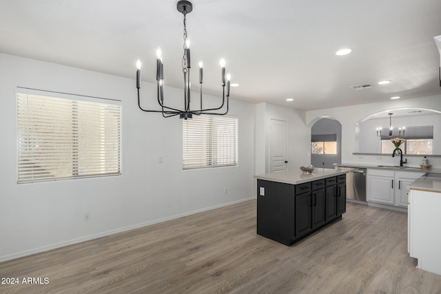 kitchen featuring arched walkways, dishwasher, light countertops, dark cabinetry, and a sink