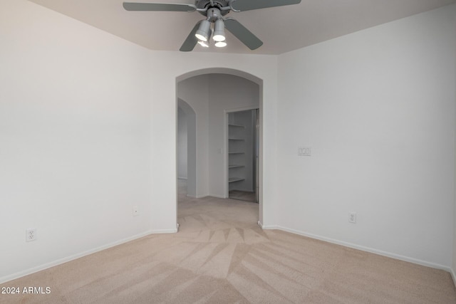 carpeted spare room with arched walkways, ceiling fan, built in shelves, and baseboards