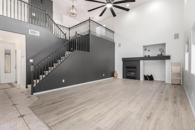 unfurnished living room with ceiling fan with notable chandelier, wood finished floors, visible vents, stairway, and a tiled fireplace