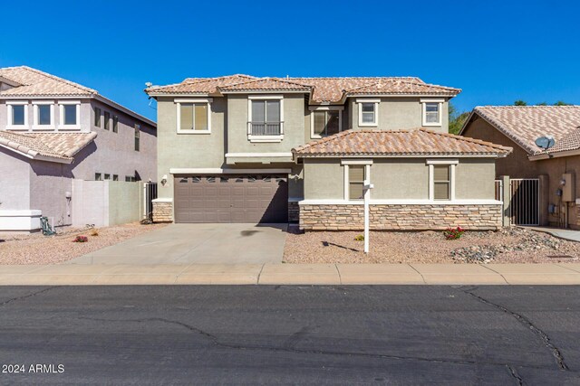 view of front of home with concrete driveway, stone siding, a tiled roof, fence, and stucco siding