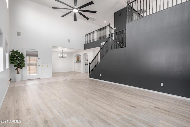 unfurnished living room featuring arched walkways, ceiling fan with notable chandelier, visible vents, wood finished floors, and stairs