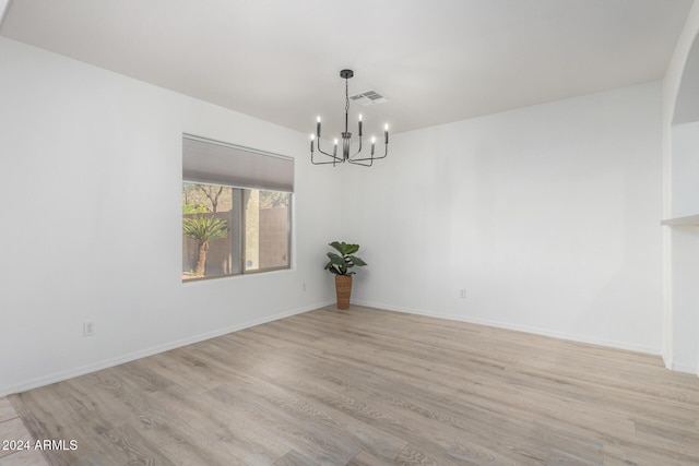 spare room featuring baseboards, light wood-style floors, visible vents, and an inviting chandelier