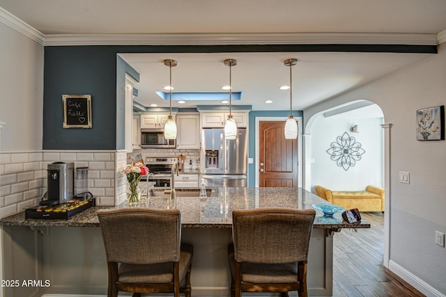 kitchen featuring a breakfast bar area, hanging light fixtures, dark stone countertops, stainless steel appliances, and backsplash