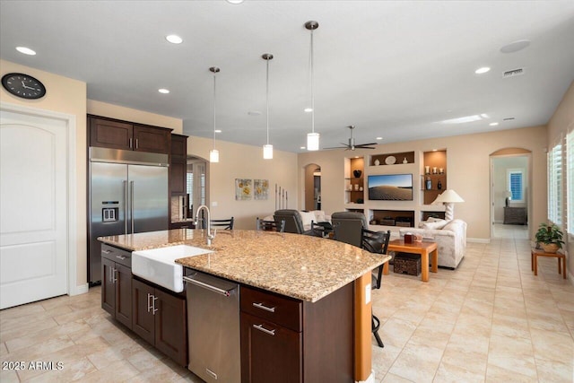 kitchen with decorative light fixtures, sink, appliances with stainless steel finishes, and a center island with sink