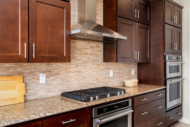 kitchen with wall chimney range hood, stainless steel appliances, light stone countertops, and tasteful backsplash