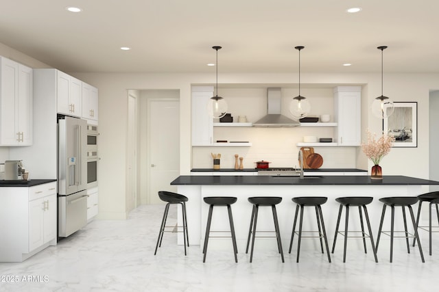 kitchen with a breakfast bar, white cabinets, wall chimney range hood, high end fridge, and pendant lighting