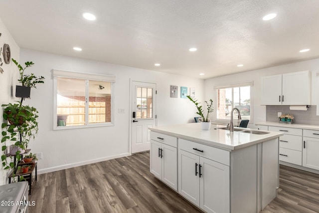 kitchen with a kitchen island with sink, a sink, dark wood-type flooring, white cabinets, and tasteful backsplash