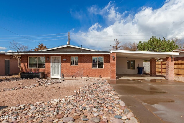 rear view of property featuring an attached carport, concrete driveway, fence, and brick siding