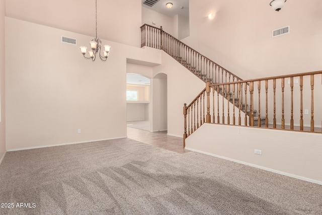 unfurnished living room with light carpet, a notable chandelier, and a towering ceiling