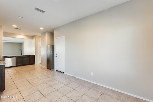 interior space with light tile patterned floors, stainless steel appliances, dark brown cabinets, light stone counters, and sink