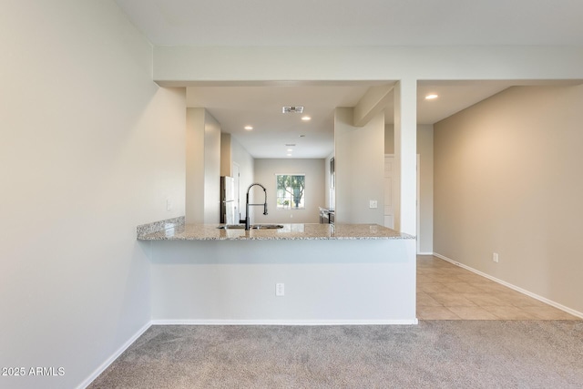 kitchen with light colored carpet, kitchen peninsula, sink, light stone counters, and white refrigerator