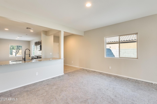 interior space with light stone counters, sink, appliances with stainless steel finishes, and light carpet