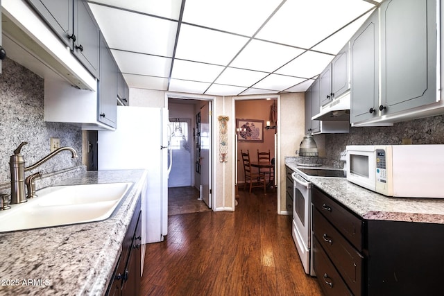 kitchen featuring under cabinet range hood, white appliances, a sink, dark wood-style floors, and tasteful backsplash