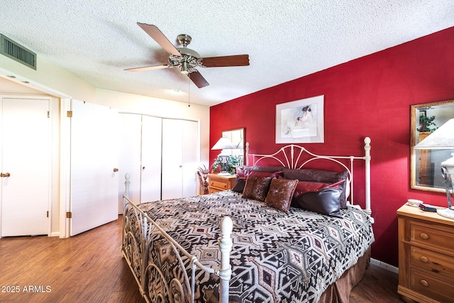 bedroom featuring a closet, visible vents, an accent wall, a textured ceiling, and wood finished floors