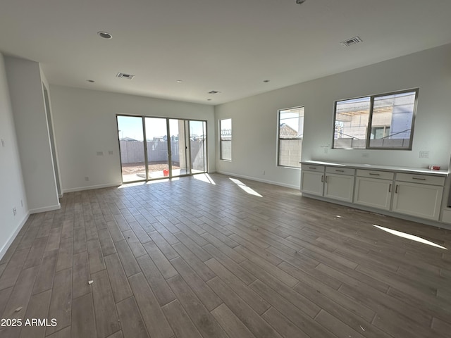 unfurnished living room with baseboards, visible vents, and dark wood-style flooring