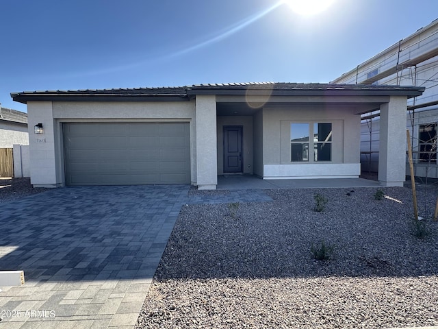 view of front facade featuring a garage, a tiled roof, decorative driveway, and stucco siding