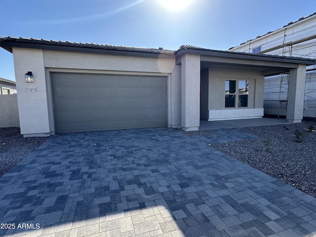 view of front of property with decorative driveway, an attached garage, a tile roof, and stucco siding