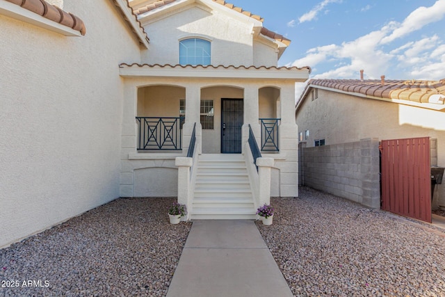 doorway to property featuring covered porch, a tiled roof, fence, and stucco siding