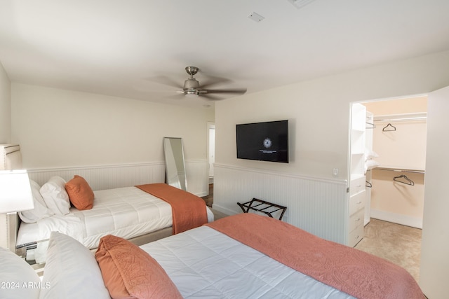 bedroom featuring light colored carpet, wooden walls, ceiling fan, a closet, and a spacious closet