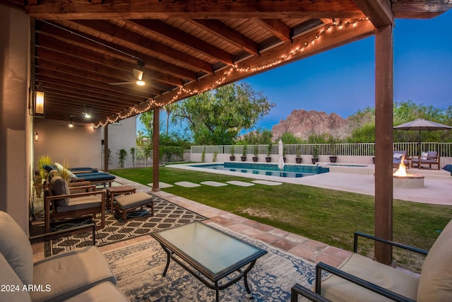 patio terrace at dusk with a mountain view, a lawn, and a fenced in pool