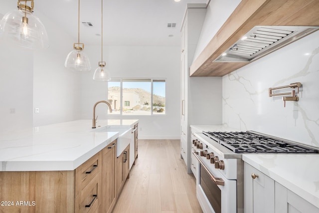 kitchen with high end white range, white cabinets, sink, light hardwood / wood-style flooring, and light stone countertops