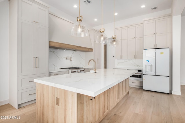 kitchen with tasteful backsplash, a large island with sink, decorative light fixtures, white cabinets, and appliances with stainless steel finishes